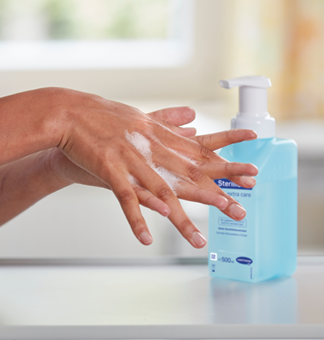 Hands that carry out hand disinfection and a Sterillium foam dispenser in the background